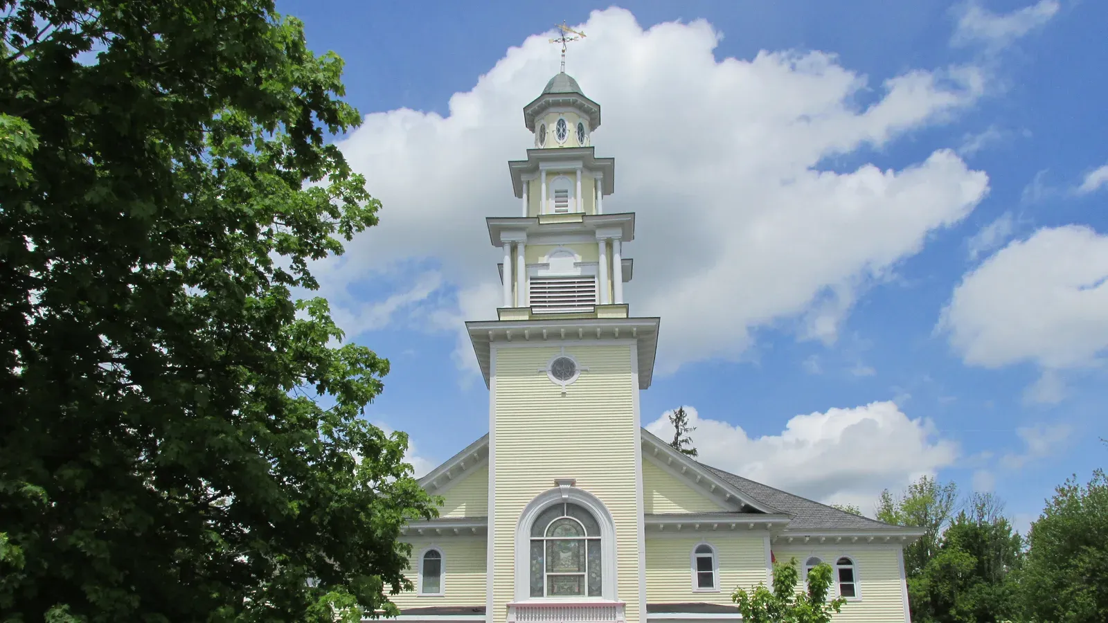 Historic yellow church with a tiered bell tower and gilded weathervane, Dracut, Massachusetts