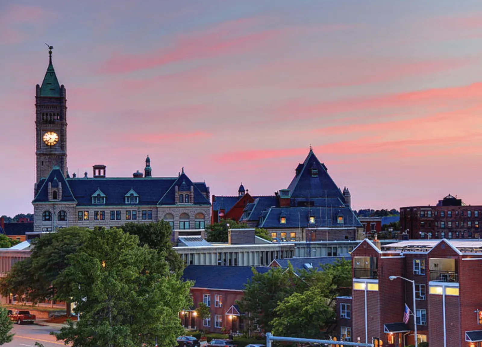 Downtown Lowell skyline at dusk with the granite City Hall clock tower rising over the brick rooftops of the mill city