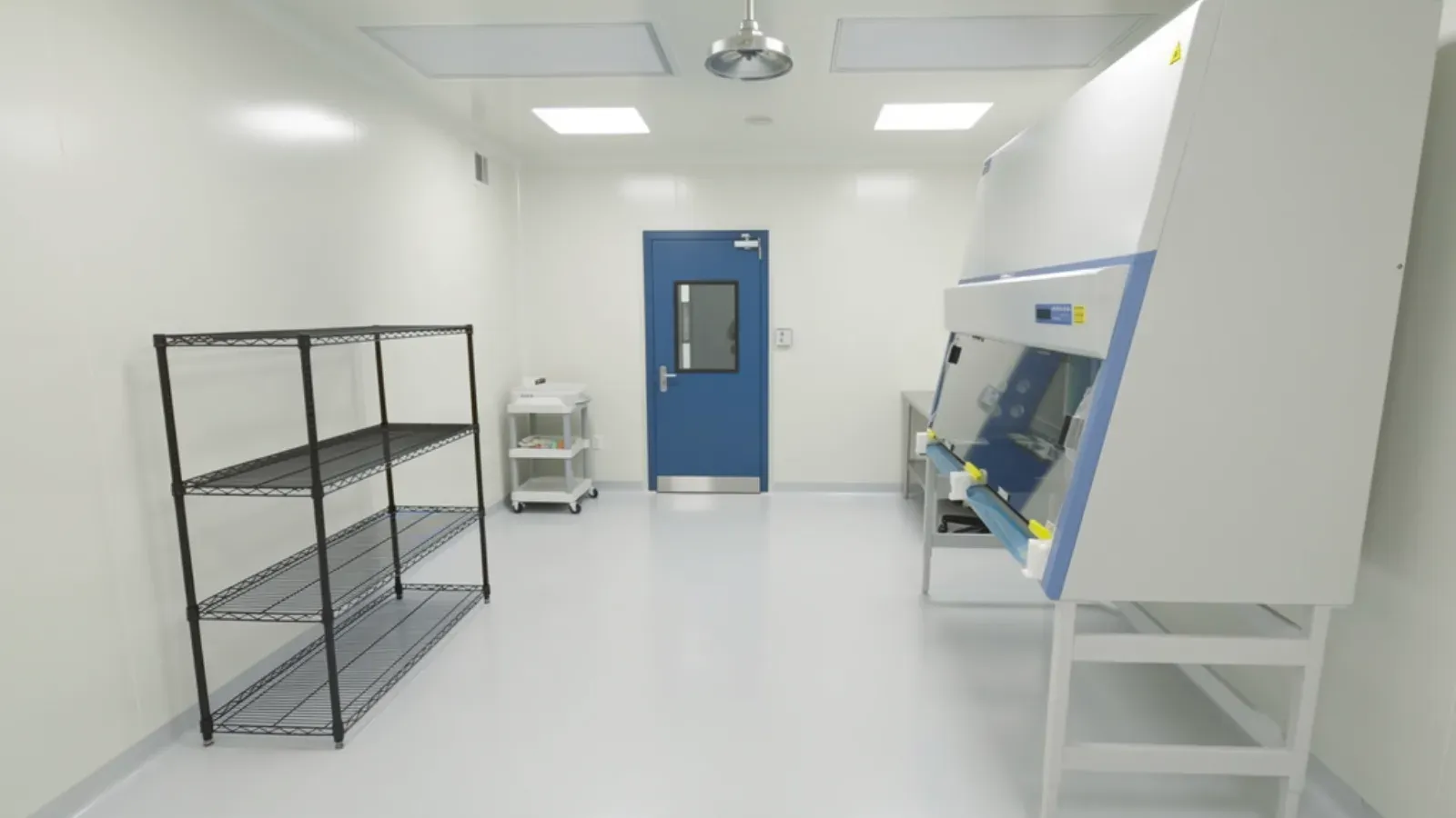 A cleanroom corridor with seamless sealed white wall panels, a coved floor and lab equipment along one side