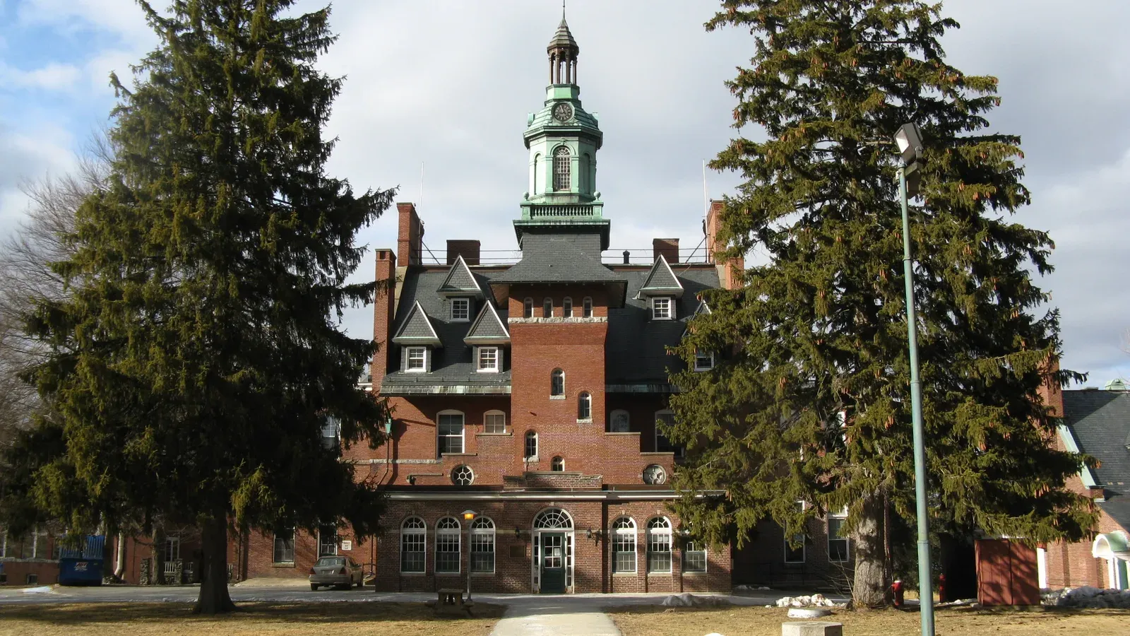 Victorian brick administration building with a green copper cupola framed by tall evergreens, Tewksbury, Massachusetts